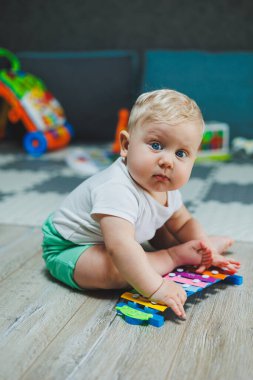 10 aylık sarı saçlı bir çocuk evde yerde oturup oyuncaklarla oynuyor. Bebekler için eğitici oyuncaklar. Çocuğun kişisel gelişimi.