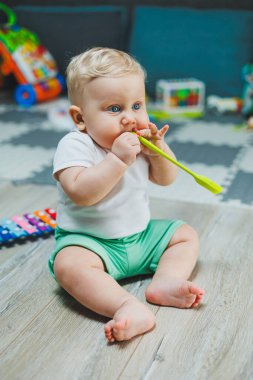 10 aylık sarı saçlı bir çocuk evde yerde oturup oyuncaklarla oynuyor. Bebekler için eğitici oyuncaklar. Çocuğun kişisel gelişimi.
