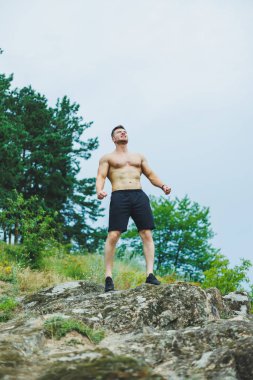 Spor kıyafetli, kaslı genç adam parkta karın kaslarını gösteriyor..