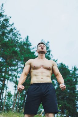 Ormanın arka planında karın kasları olan genç bir adam. Kayalık zeminde atletik şişmiş bir adam.