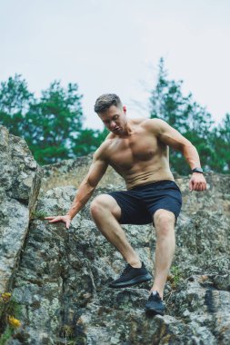 Spor kıyafetli, kaslı genç adam parkta karın kaslarını gösteriyor..