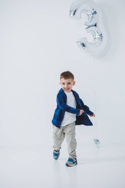 Beyaz arka planda gömleği ve pantolonu olan, şişme topu olan 3 yaşında şık bir çocuk. Yüzünde bir gülümsemeyle neşeli bir çocuk.