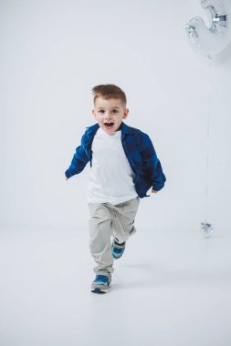 Beyaz arka planda gömleği ve pantolonu olan, şişme topu olan 3 yaşında şık bir çocuk. Yüzünde bir gülümsemeyle neşeli bir çocuk.