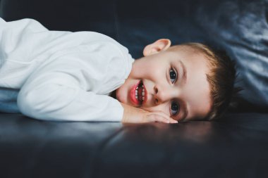 Yüzünde gülümseme olan beyaz kazak ve pantolon giymiş 3 yaşında bir çocuk. Şık giyinmiş küçük çocuk..