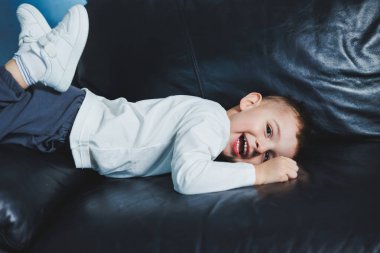 Yüzünde gülümseme olan beyaz kazak ve pantolon giymiş 3 yaşında bir çocuk. Şık giyinmiş küçük çocuk..