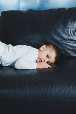 Yüzünde gülümseme olan beyaz kazak ve pantolon giymiş 3 yaşında bir çocuk. Şık giyinmiş küçük çocuk..