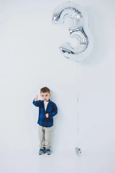 stock image A stylish 3-year-old boy in a shirt and pants on a white background with an inflatable ball. Cheerful boy with a smile on his face.