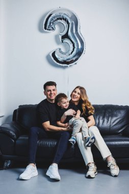 Genç evli bir çift oğullarına sarılıyor. Anne, baba ve oğul kanepede oturuyor. Mutlu bir aile..