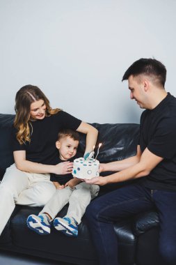 Genç evli bir çift oğullarına sarılıyor. Anne, baba ve oğul kanepede oturuyor. Mutlu bir aile..