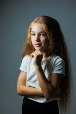 Uzun kıvırcık saçlı, kot pantolonlu beyaz tişörtlü güzel bir kız. Kızın yüzünde farklı duygular var..