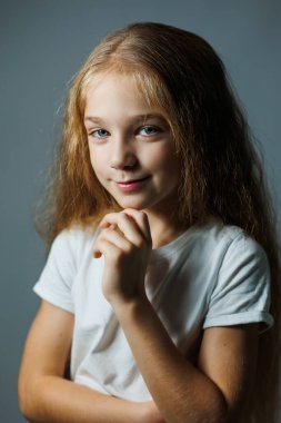 Uzun kıvırcık saçlı, kot pantolonlu beyaz tişörtlü güzel bir kız. Kızın yüzünde farklı duygular var..