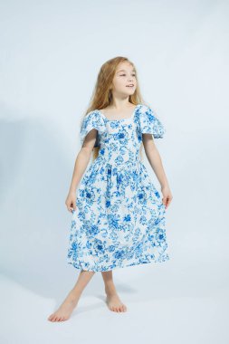 Yazlık elbiseli küçük bir kız beyaz arka planda kameraya poz veriyor. Kızlar için yaz giysileri.