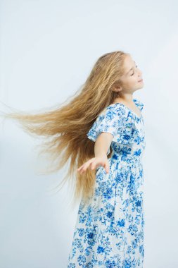 Yazlık elbiseli küçük bir kız beyaz arka planda kameraya poz veriyor. Kızlar için yaz giysileri.