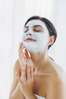 Yüzünde beyaz bir maske olan bir kadının yakın çekimi. Güzellik salonundaki müşterinizin yüzündeki maske. Cilt temizleme ve nemlendirici konsept. Yüz bakımı.