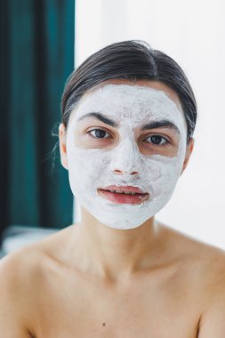 Yüzünde beyaz bir maske olan bir kadının yakın çekimi. Güzellik salonundaki müşterinizin yüzündeki maske. Cilt temizleme ve nemlendirici konsept. Yüz bakımı.