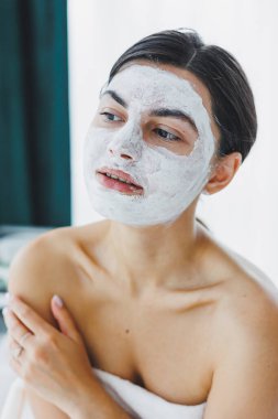 Yüzünde beyaz bir maske olan bir kadının yakın çekimi. Güzellik salonundaki müşterinizin yüzündeki maske. Cilt temizleme ve nemlendirici konsept. Yüz bakımı.