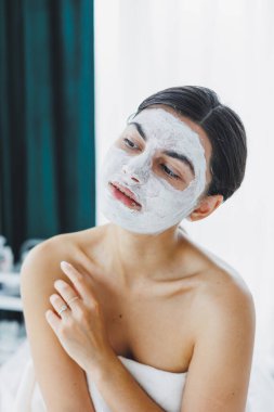 Yüzünde beyaz bir maske olan bir kadının yakın çekimi. Güzellik salonundaki müşterinizin yüzündeki maske. Cilt temizleme ve nemlendirici konsept. Yüz bakımı.