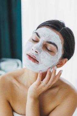 Yüzünde beyaz bir maske olan bir kadının yakın çekimi. Güzellik salonundaki müşterinizin yüzündeki maske. Cilt temizleme ve nemlendirici konsept. Yüz bakımı.