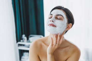 Yüzünde beyaz bir maske olan bir kadının yakın çekimi. Güzellik salonundaki müşterinizin yüzündeki maske. Cilt temizleme ve nemlendirici konsept. Yüz bakımı.