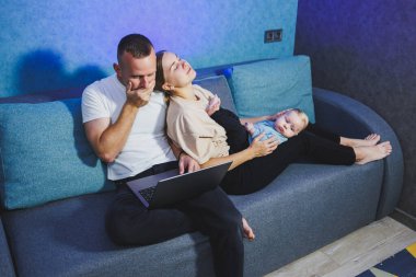 Genç evli bir çift modern oturma odasında sevimli küçük bir bebekle oynarken eğleniyor. Gülümseyen ebeveynler, anne ve baba, oğullarıyla evde vakit geçirmekten zevk alıyorlar.