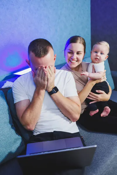 Stock image Smiling parents on sofa in living room with little baby son watching video together having fun with modern laptop. Happy young family with little boy watching funny video on computer