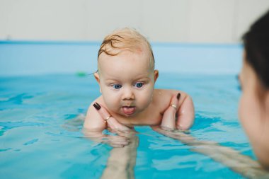 Bir bebek havuzda koçla yüzmeyi öğrenir. Küçük çocuklar için yüzme kursları. Çocuklar için yüzme havuzu