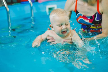 Bir bebek havuzda koçla yüzmeyi öğrenir. Küçük çocuklar için yüzme kursları. Çocuklar için yüzme havuzu