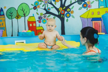 Havuzdaki küçük çocuk. Bir bebek havuzda koçla yüzmeyi öğrenir. Küçük çocuklar için yüzme kursları. Çocuklar için yüzme havuzu