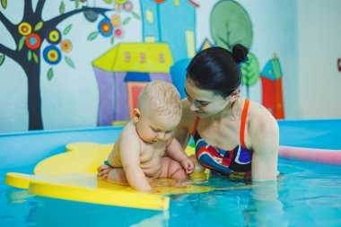 Havuzdaki küçük çocuk. Bir bebek havuzda koçla yüzmeyi öğrenir. Küçük çocuklar için yüzme kursları. Çocuklar için yüzme havuzu