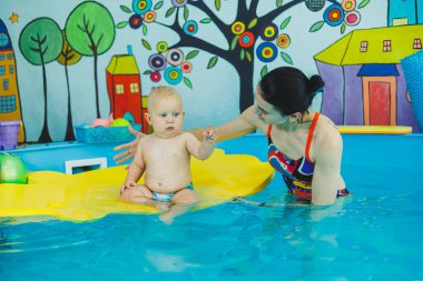 Havuzdaki küçük çocuk. Bir bebek havuzda koçla yüzmeyi öğrenir. Küçük çocuklar için yüzme kursları. Çocuklar için yüzme havuzu