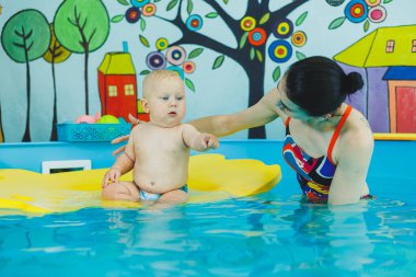 Havuzdaki küçük çocuk. Bir bebek havuzda koçla yüzmeyi öğrenir. Küçük çocuklar için yüzme kursları. Çocuklar için yüzme havuzu
