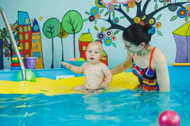 Çocuklar için yüzme havuzu. Havuzdaki küçük çocuk. Bir bebek havuzda koçla yüzmeyi öğrenir. Küçük çocuklar için yüzme kursu.