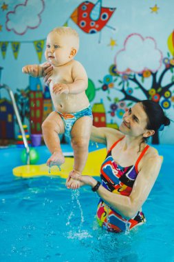 Çocuklar için yüzme havuzu. Havuzdaki küçük çocuk. Bir bebek havuzda koçla yüzmeyi öğrenir. Küçük çocuklar için yüzme kursu.
