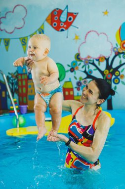 Çocuklar için yüzme havuzu. Havuzdaki küçük çocuk. Bir bebek havuzda koçla yüzmeyi öğrenir. Küçük çocuklar için yüzme kursu.