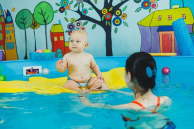 Çocuklar için yüzme havuzu. Havuzdaki küçük çocuk. Bir bebek havuzda koçla yüzmeyi öğrenir. Küçük çocuklar için yüzme kursu.