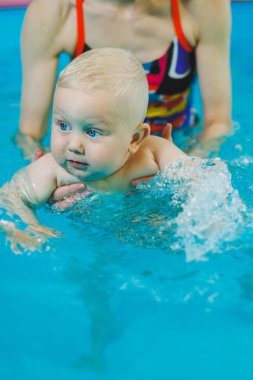 Havuzdaki küçük çocuk. Bir bebek havuzda koçla yüzmeyi öğrenir. Küçük çocuklar için yüzme kursları. Çocuklar için yüzme havuzu