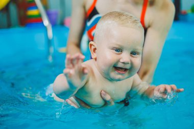 Havuzdaki küçük çocuk. Bir bebek havuzda koçla yüzmeyi öğrenir. Küçük çocuklar için yüzme kursları. Çocuklar için yüzme havuzu