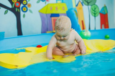 Bir bebek havuzda koçla yüzmeyi öğrenir. Küçük çocuklar için yüzme kursları. Bebek havuzda yüzüyor..