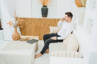 Genç bir adam evinde kanepede oturuyor ve uzaktan bilgisayarla çalışıyor..