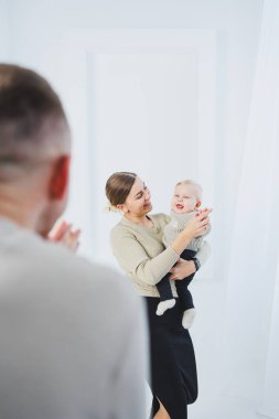 Genç ebeveynler, anne ve baba beyaz arka planda bir bebekle oynuyorlar. Evli bir çift yeni doğan oğullarına sarılıyor. Mutlu bir aile..