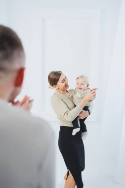 Genç ebeveynler, anne ve baba beyaz arka planda bir bebekle oynuyorlar. Evli bir çift yeni doğan oğullarına sarılıyor. Mutlu bir aile..