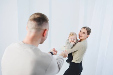 Genç ebeveynler, anne ve baba beyaz arka planda bir bebekle oynuyorlar. Evli bir çift yeni doğan oğullarına sarılıyor. Mutlu bir aile..