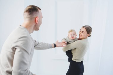 Genç ebeveynler, anne ve baba beyaz arka planda bir bebekle oynuyorlar. Evli bir çift yeni doğan oğullarına sarılıyor. Mutlu bir aile..