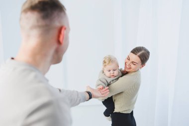 Genç ebeveynler, anne ve baba beyaz arka planda bir bebekle oynuyorlar. Evli bir çift yeni doğan oğullarına sarılıyor. Mutlu bir aile..