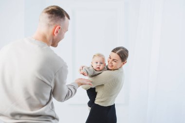 Genç ebeveynler, anne ve baba beyaz arka planda bir bebekle oynuyorlar. Evli bir çift yeni doğan oğullarına sarılıyor. Mutlu bir aile..