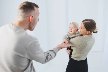 Genç ebeveynler, anne ve baba beyaz arka planda bir bebekle oynuyorlar. Evli bir çift yeni doğan oğullarına sarılıyor. Mutlu bir aile..