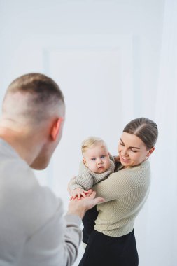 Genç ebeveynler, anne ve baba beyaz arka planda bir bebekle oynuyorlar. Evli bir çift yeni doğan oğullarına sarılıyor. Mutlu bir aile..