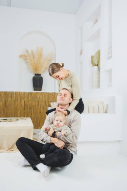 Evde kucağında bebek olan bir aile. Mutlu, genç bir aile babası ve yeni doğmuş bir bebek gülümsüyor ve arka planda öpüşüyor, evde sevgi dolu bir aile.