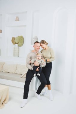 Evde kucağında bebek olan bir aile. Mutlu, genç bir aile babası ve yeni doğmuş bir bebek gülümsüyor ve arka planda öpüşüyor, evde sevgi dolu bir aile.