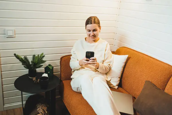 Stock image A woman in home clothes is sitting at home on the sofa with a laptop and talking on the phone. Work from home.